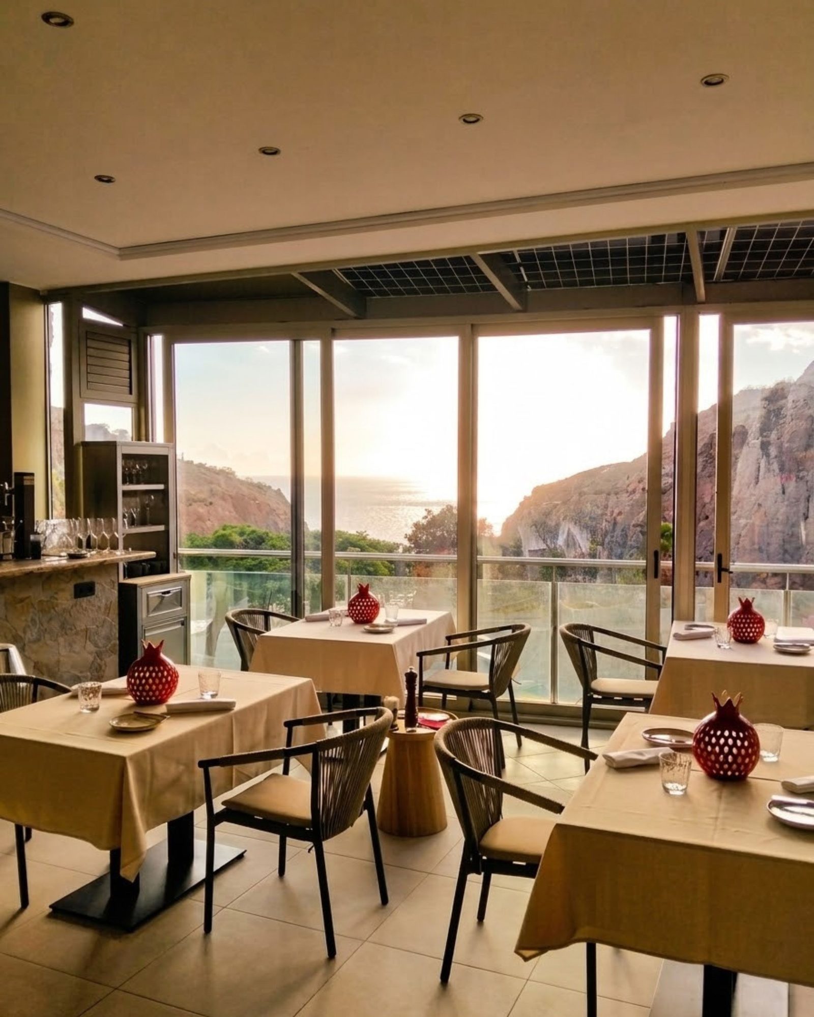 Comedor de La Granada GRX al atardecer, con granadas rojas sobre las mesas y vistas al mar y al acantilado de Amadores