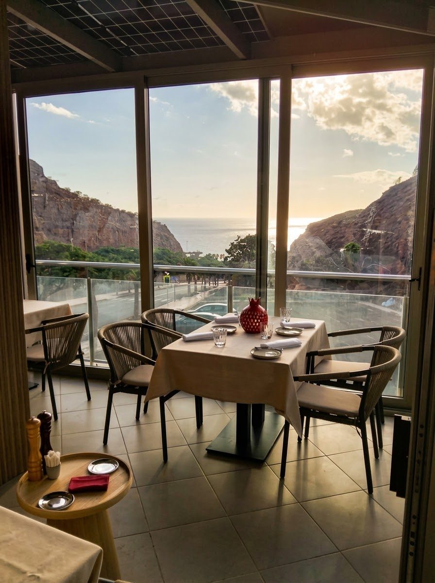 Mesa para dos junto al ventanal de La Granada GRX, con vistas al acantilado y al mar de Amadores al atardecer